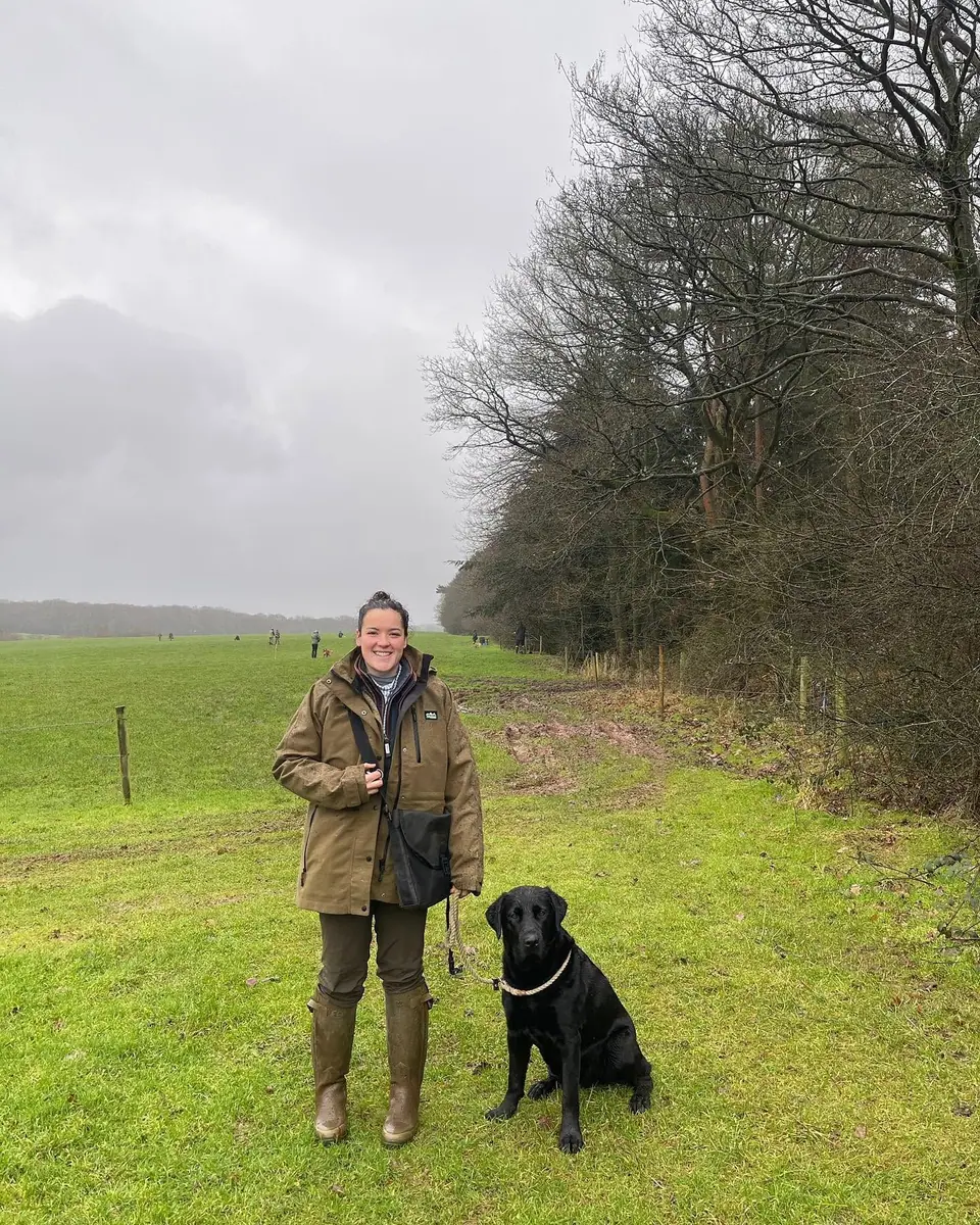 Kate standing in a field with her black Labrador, Billy