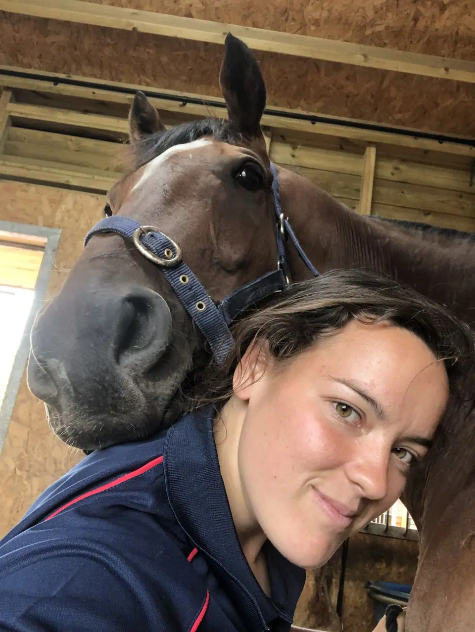 Kate smiling, cheek to cheek with a bay horse in a navy headcollar