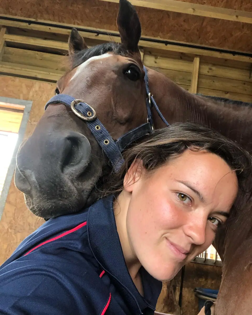 Kate with a bay racehorse resting its head on her shoulder